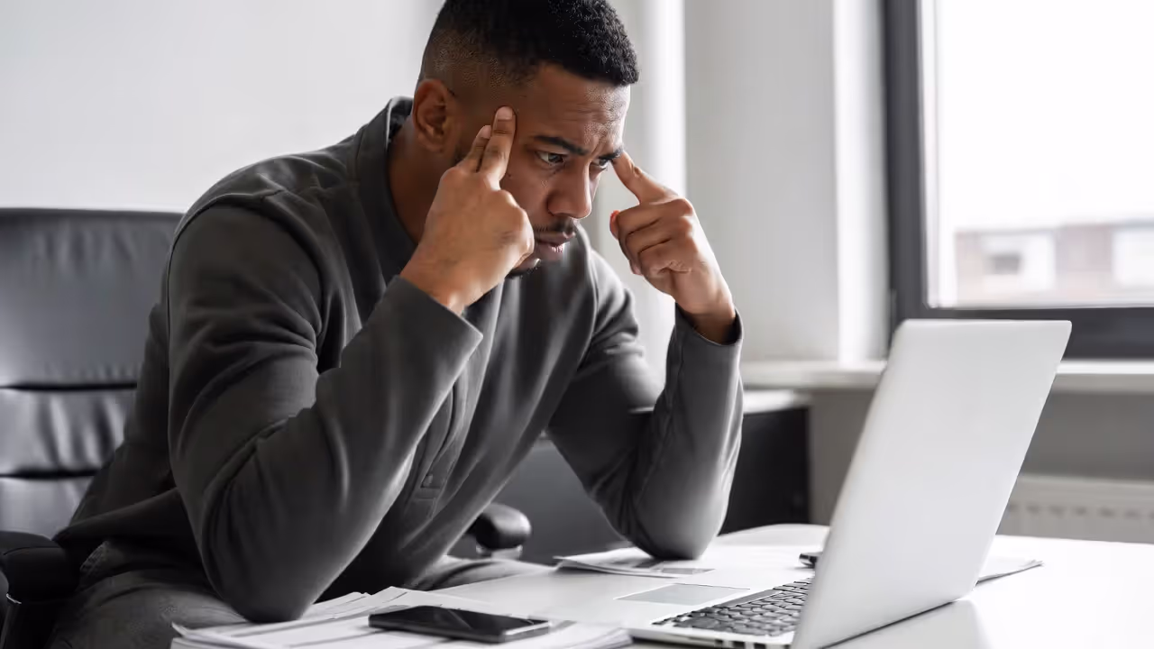 Stressed professional sitting at a desk with laptop and paperwork
