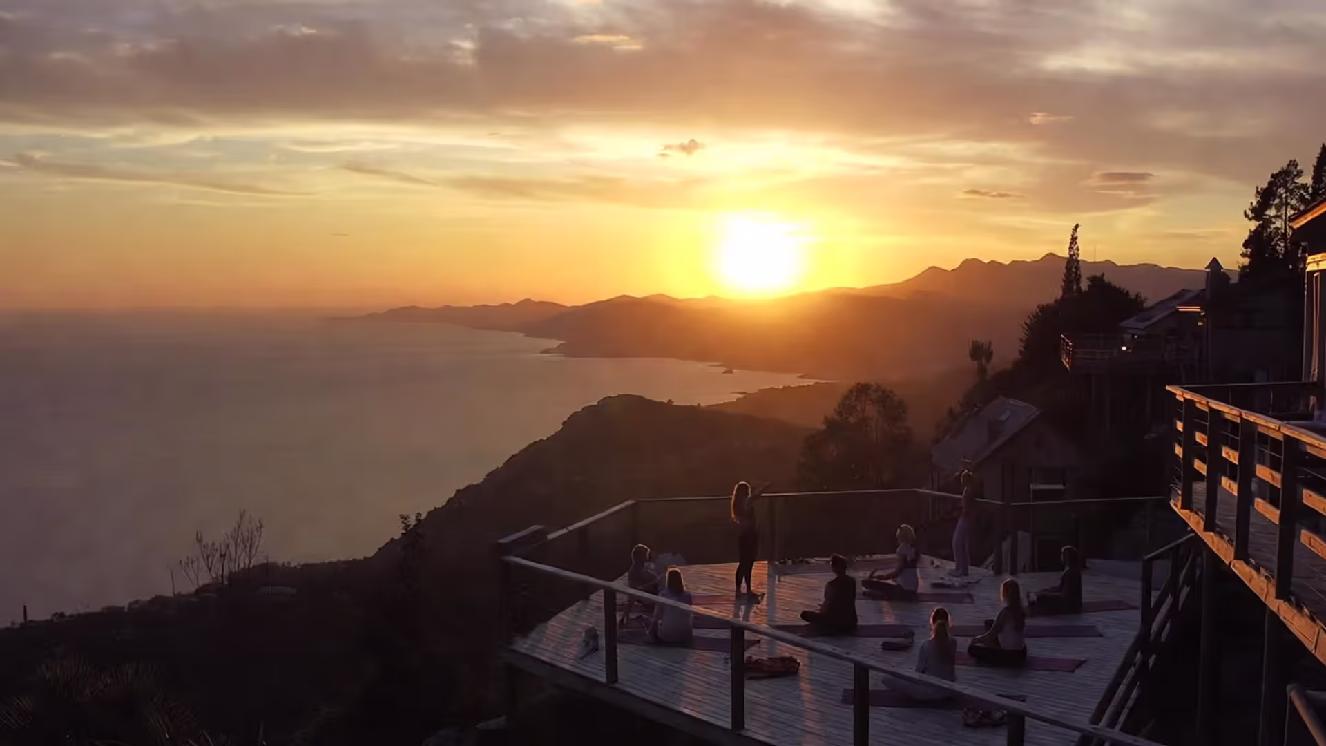 Group practicing yoga at sunset on an outdoor deck at a retreat center.
