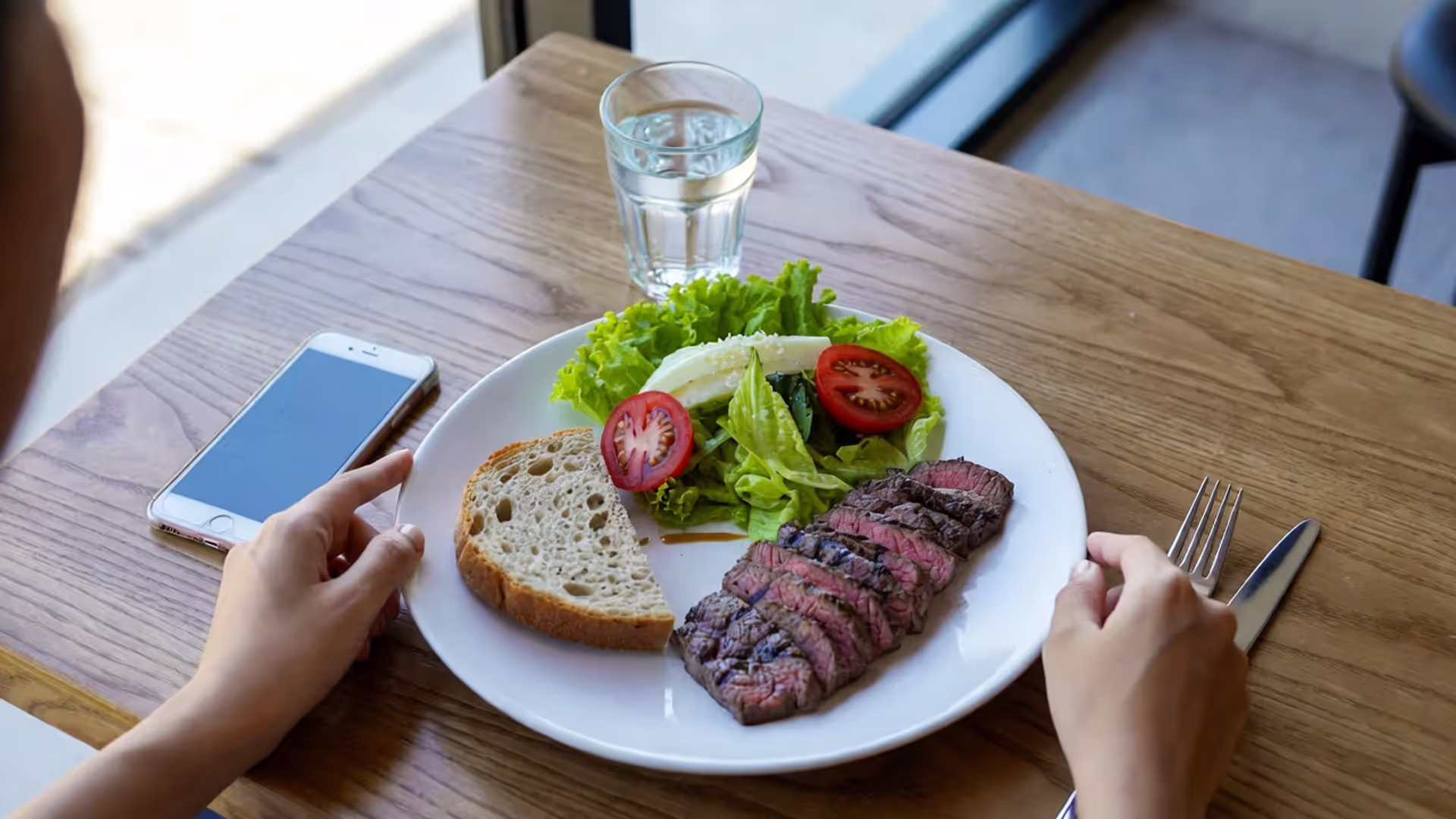 Meal on a table with a phone placed away and hands resting before eating.